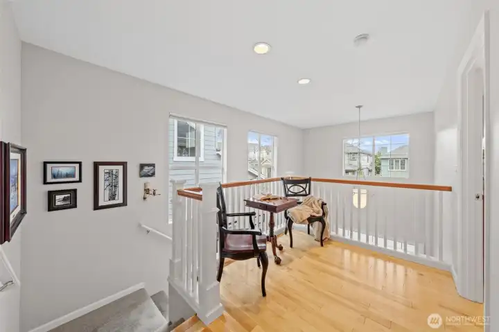 This upper landing creates a bright and comfortable flex space, ideal for reading, relaxing, or working from home. Multiple windows fill the area with natural light, highlighting the open railing design and the home’s warm, inviting atmosphere.