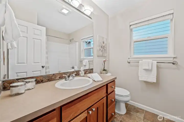 The main bath offers a clean and functional layout with a spacious vanity and warm wood cabinetry that provides excellent storage. A large mirror and bright lighting enhance the room, while the tub/shower combo and vinyl flooring add everyday convenience and durability.