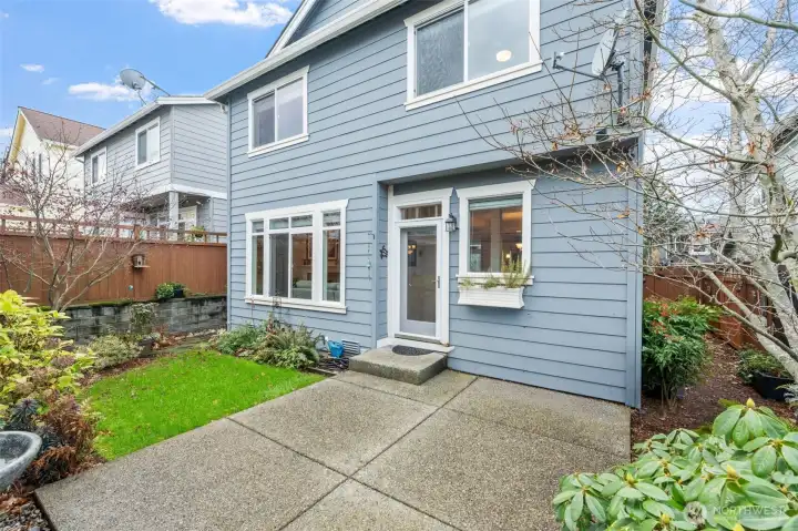 The back patio offers a welcoming outdoor extension of the home, surrounded by mature landscaping and space for relaxing or entertaining. The door creates a seamless connection between the indoors and outdoors, making it easy to step outside and enjoy fresh air anytime.