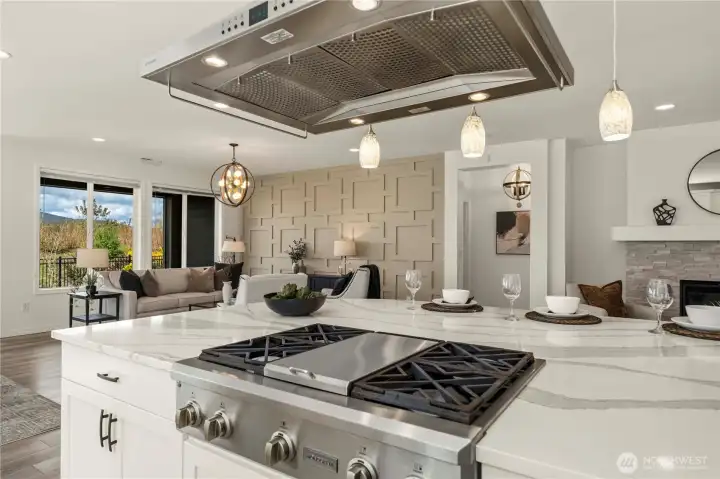 This stunning kitchen overlooking the great room w/ gorgeous lighting, decorative custom wall, stacked stone fireplace and the beautiful outdoor space.