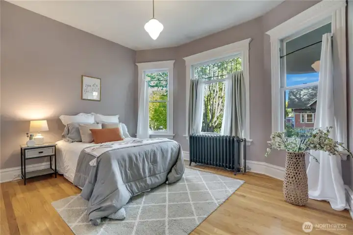 A door from the linen area opens into this front bedroom with bay windows, high ceilings, and oak floors.