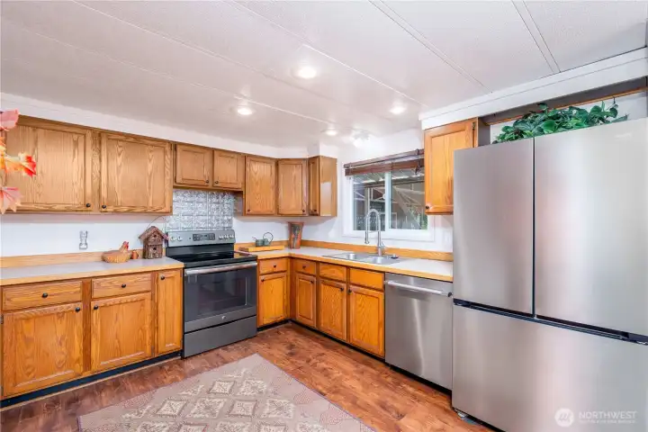 Bright and functional kitchen featuring abundant oak cabinetry, generous counter space, and updated stainless steel appliances. A large window above the sink brings in natural light and offers views of the covered outdoor area and backyard beyond. The efficient layout provides excellent storage and workspace, while durable flooring and timeless finishes create a warm, welcoming heart of the home for everyday living and entertaining.