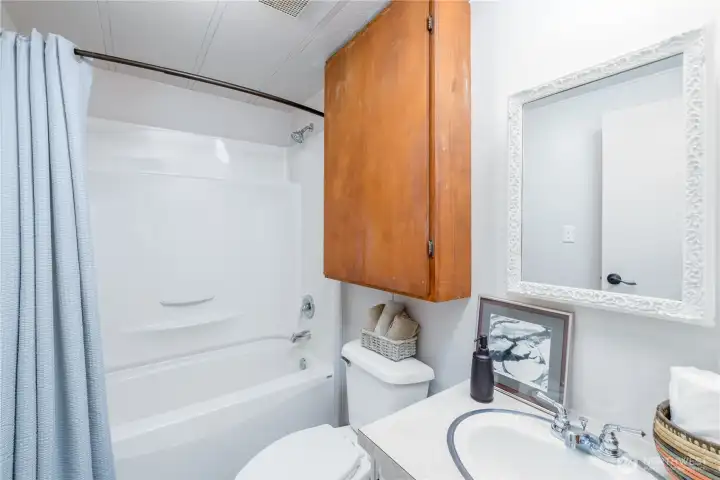 Bright and functional bathroom featuring a tub/shower combination with a clean, low-maintenance surround, ample storage with an overhead cabinet, and a neutral color palette that complements a variety of styles.