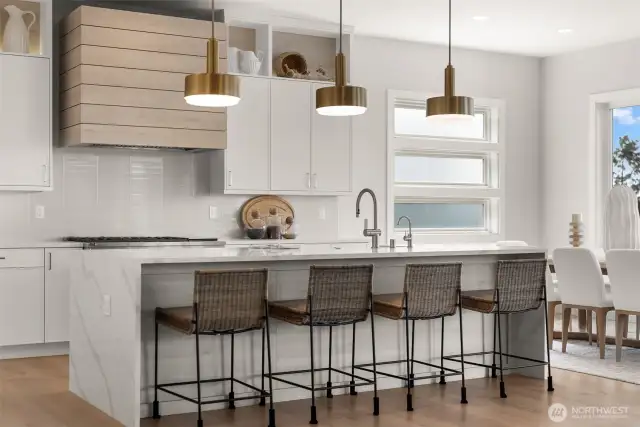 A custom-wrapped range hood, ceiling-height cabinetry, and horizontally stacked windows flood the space with natural light—blending form, function, and style seamlessly.
