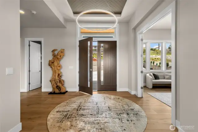 A stunning 8-foot modern front door opens to a grand entryway with a view of the Puget Sound, featuring a custom ceiling inlay that sets the tone for the refined design found throughout the home.