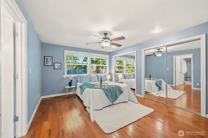 Spacious principal bedroom with large windows, mirrored closet doors, and ceiling fan.
