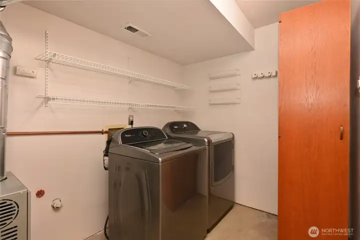 In the lower level laundry room are the large-capacity Whirlpool washer and dryer. The shelving unit will stay. A new Trane RunTru furnace was installed in June 2026. Unshown on the left is more storage space.