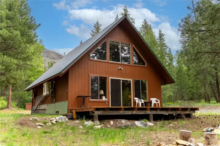 Spacious front deck creates the perfect outdoor living space for morning coffee, summer dinners, or relaxing beneath the pines while overlooking the peaceful seasonal irrigation ditch and fire pit area.