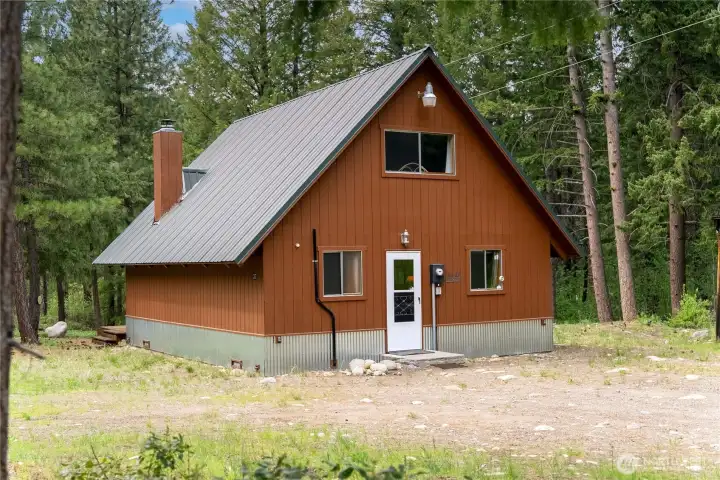 Side view of the cabin showcasing the low-maintenance exterior, wooded privacy, and rustic storage/woodshed area.