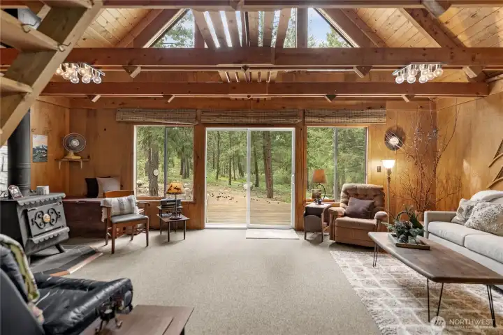 Light-filled living area with dramatic wall of windows and sliding glass doors opening to the deck and peaceful forest surroundings.