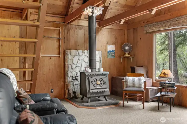 Cozy great room featuring soaring vaulted ceilings, exposed timber beams, and a charming freestanding wood stove that creates the perfect mountain cabin atmosphere.
