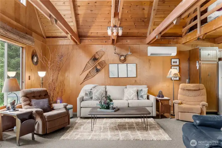 Expansive great room with vaulted tongue-and-groove ceilings, wood stove centerpiece, and seamless indoor-outdoor connection to the surrounding natural setting.