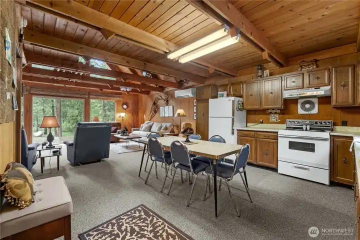 Rustic cabin-style kitchen featuring exposed wood beams, classic wood cabinetry, and an open dining space that blends seamlessly with the living area.