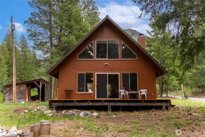 Storybook A-frame cabin surrounded by towering evergreens with timeless mountain charm, soaring windows, and a durable metal roof designed for all-season enjoyment.