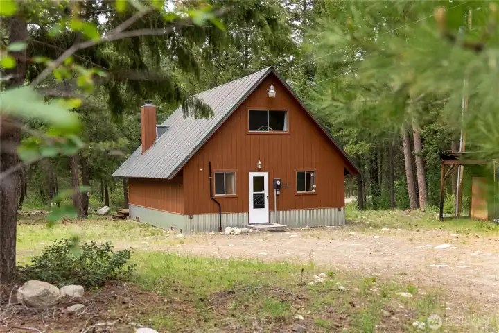 Side exterior view highlights the cabin’s private setting, easy-access layout, and additional covered storage/woodshed space ideal for mountain living.