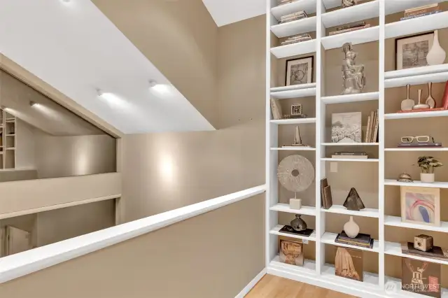 Stepping out to the cozy loft where a dramatic floor-to-ceiling bookcase is the perfect spot to enjoy a book while looking out the windows to nature