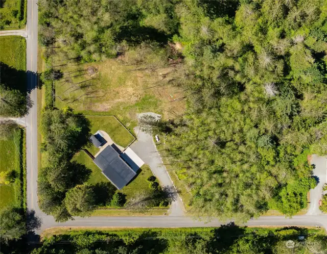 Aerial view of buildings, corner lot, grassy area and partially wooded area.  Area to the right has wetlands and is a protected critical area.