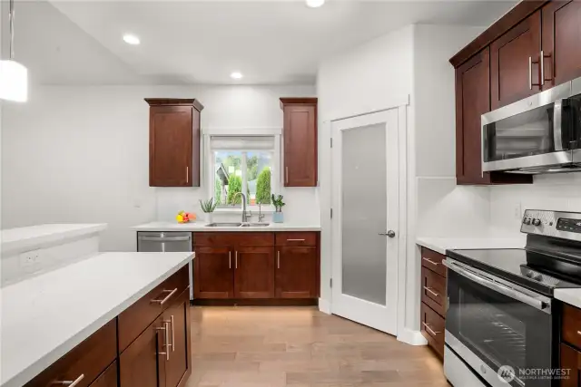 Modern kitchen with stainless steel appliances, quartz countertops, rich wood cabinetry, and a walk-in pantry behind a frosted glass door.