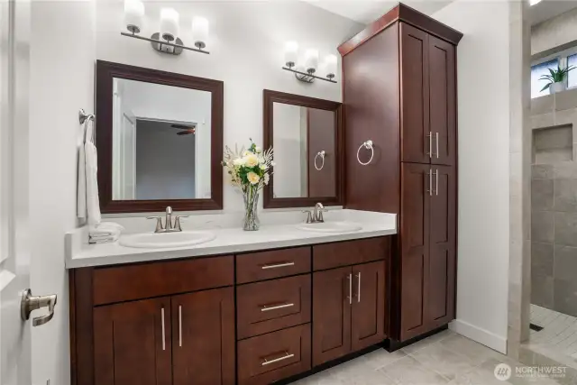 Luxurious primary en-suite bath with dual sinks, rich wood cabinetry, quartz countertops, and a walk-in tiled shower.