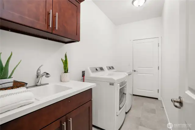 Well-appointed laundry room on the main floor with utility sink, overhead cabinetry, and washer/dryer included.
