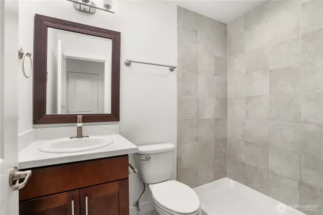 Upstairs 3/4 bath featuring a tiled shower, quartz countertop vanity, and rich wood cabinetry.