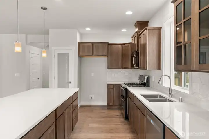 Kitchen features quartz counters and maple cabinets that are stained in graphite and full backsplash.