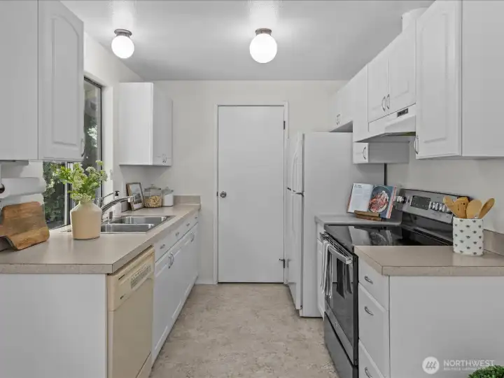 Functional galley kitchen featuring all the essentials: dishwasher, microwave, refrigerator, and stove — perfect for everyday cooking.