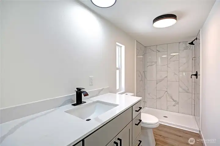 Beautiful primary bath with tiled shower, quartz countertops, and large vanity.
