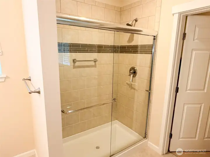 Attractively tiled shower with grab bar, and door to the walk-in closet.