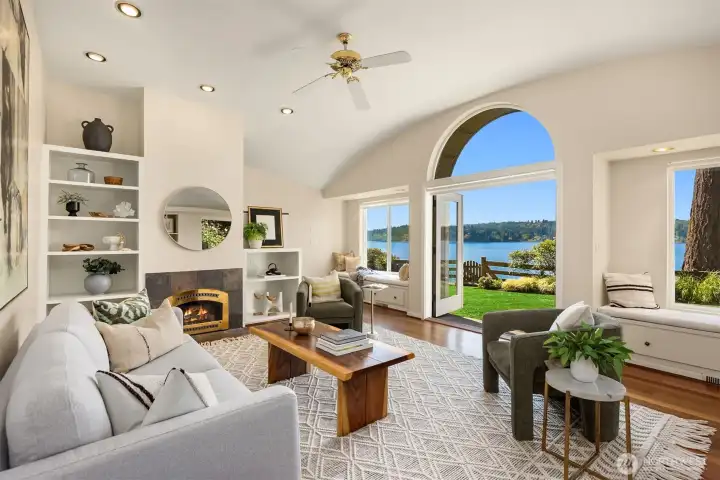 Bright living room featuring vaulted ceilings, cozy fireplace, built-in shelving, and French doors that frame beautiful water views and seamless indoor-outdoor flow.