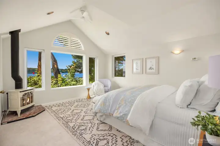 Inviting primary retreat with vaulted ceilings, warm gas stove, and picturesque water views creating a calm and restful setting.
