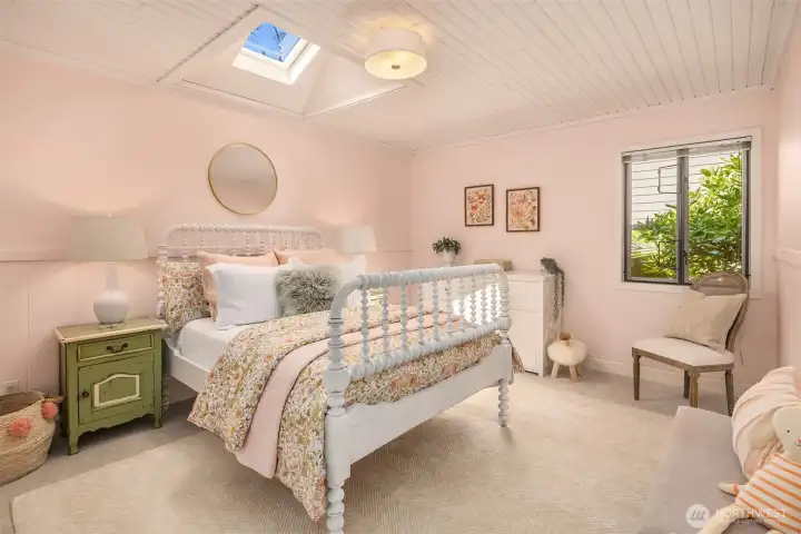 In the opposite wing from the primary is this light-filled bedroom with skylight, soft tones, and a warm, comfortable atmosphere.