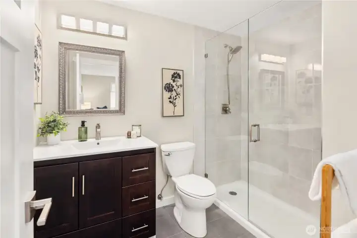 This remodeled primary bathroom includes spacious walk-in glass shower with floor-to-ceiling tile