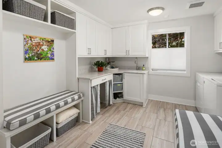 The Mud / Laundry Room.  A perfect landing spot for coats and shoes.  Easy clean tile floor, cutom bench seating with coat hooks on 1 side.  The folding counter has quartz counters, custom cabinets above for lots of storage a sink and and area that could be designated for your dog or cat.