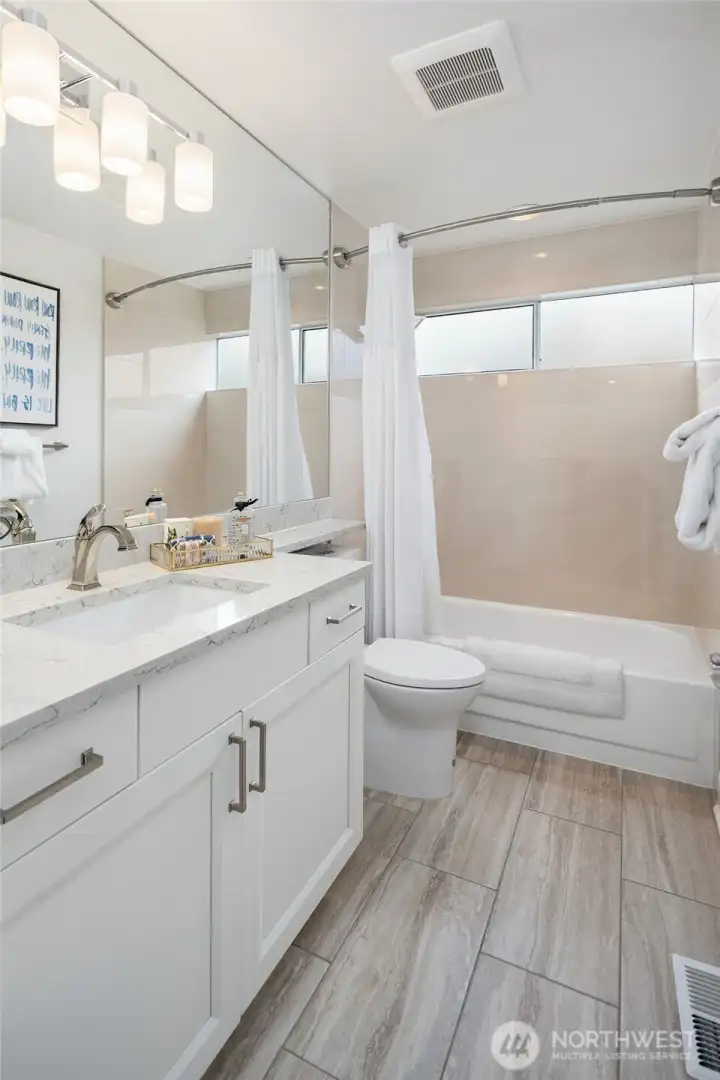 The hall bath has tile floors, custom Belmont Cabinet with drawers, Under mount sink.  A full wall mirror with lighting, quartz counters with a banjo shelf over the toilet, a shower/Tub with a custom tile wall.