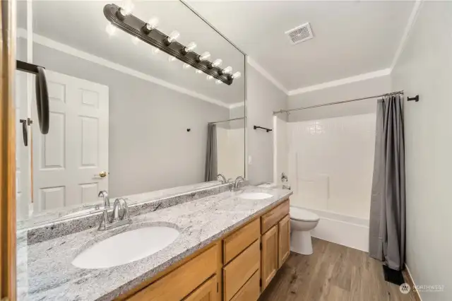 2nd level hall bathroom with new granite countertops, new double sinks and faucets in 2023. Custom Mirror, lighting and new plank flooring in 2023.