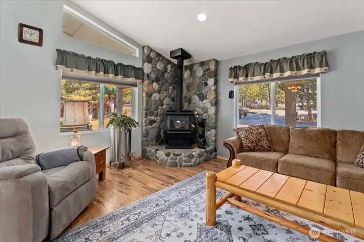 Corner woodstove set on a floor-to-ceiling river rock hearth and surround.
