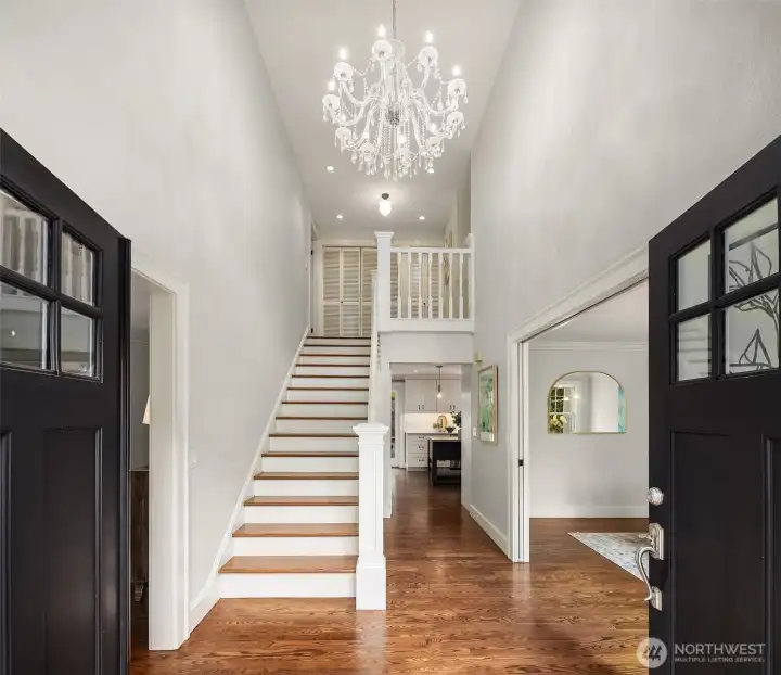 Welcome home! Double black doors swing open from the columned portico to reveal the staircase and hardwood floors within — the transition from outside to inside feels intentional at every step