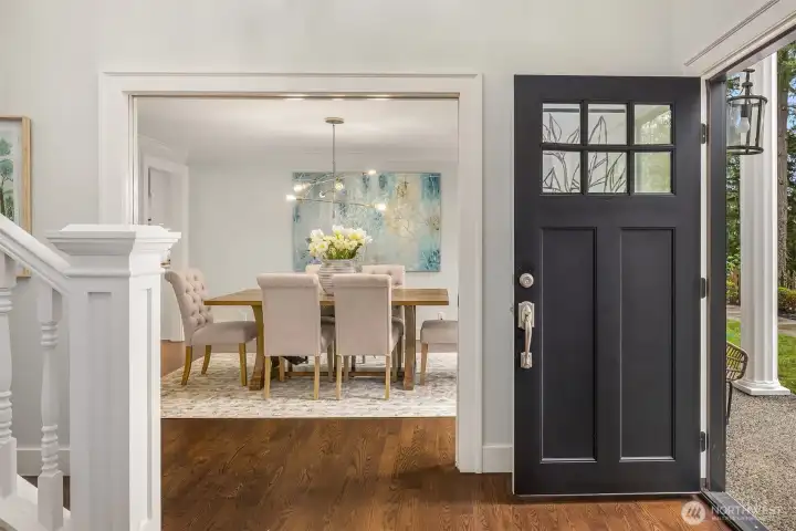 Classic colonial entry with bold black front door, white millwork staircase, rich hardwood floors, and an immediate sight line into the formal dining room — a proper welcome home