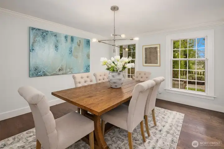 Formal dining room with crown molding, statement chandelier, hardwood floors, and serene garden views