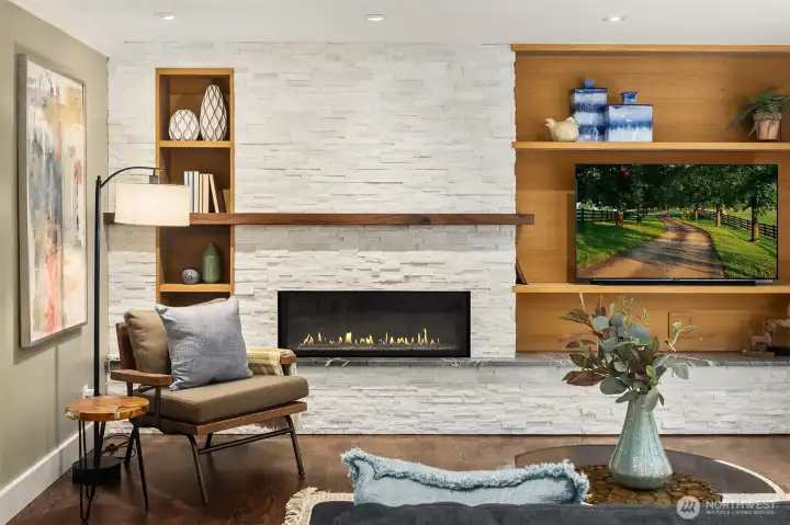 Linear gas fireplace with full-height stacked stone surround, live-edge wood mantle, and custom warm-toned built-ins — the heart of the main living area