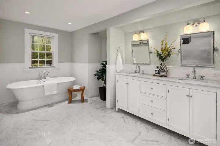 Stunning primary bath featuring freestanding soaking tub, dual vanity with marble countertops, marble tile floors, and subway tile wainscoting