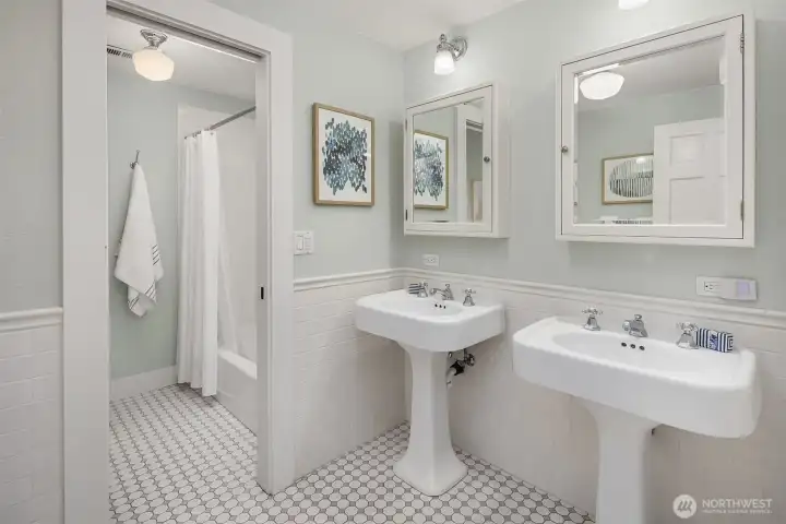 Full bath with dual pedestal sinks, penny tile floors, subway tile wainscoting, and separate tub/shower