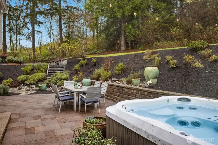 The rear grounds in full — a sprawling lawn, private patio, hot tub, and mature tree canopy that makes every warm day feel like a long weekend