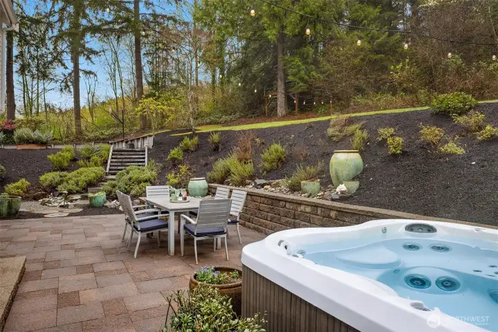 The rear grounds in full — a sprawling lawn, private patio, hot tub, and mature tree canopy that makes every warm day feel like a long weekend
