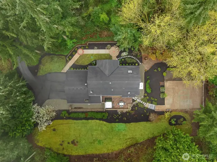 Aerial overhead showing the full property footprint — main residence, attached garage, rear patio, sports court, front circular path, and the mature tree canopy surrounding it all