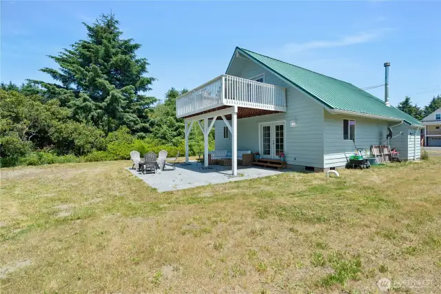 Back of home with large yard, upper deck, and lower patio area