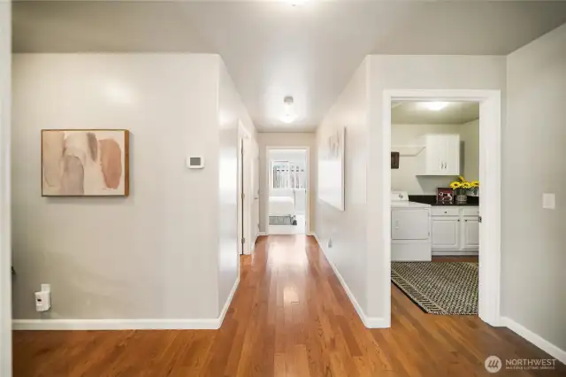 This view highlights the spacious pathway leading to the utility room and garage access, with the primary bedroom to the left and the second bedroom and full bath straight ahead.