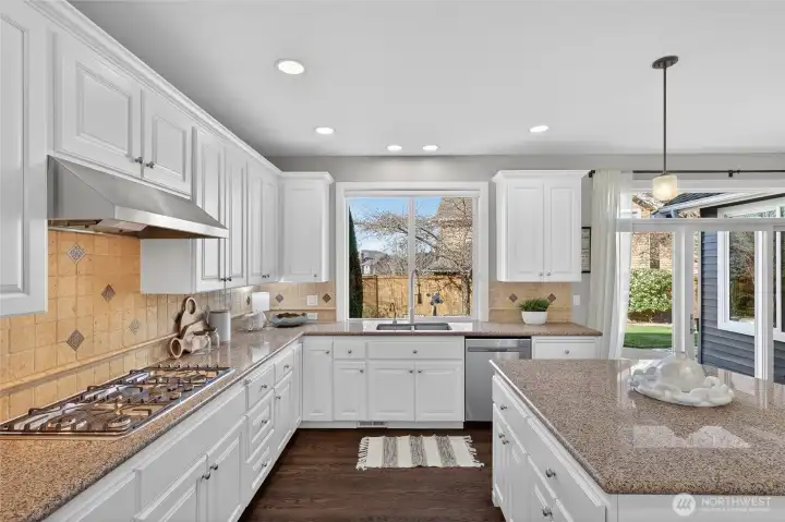 Spacious kitchen with white cabinets, slab granite, and new cooktop, dishwasher, and fridge.
