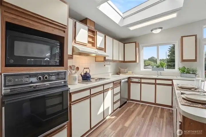 Spacious gourmet kitchen features new LVP flooring, skylights, wall oven, cooktop, western exposure and eating bar opening to the family room.  Virtually staged photo.
